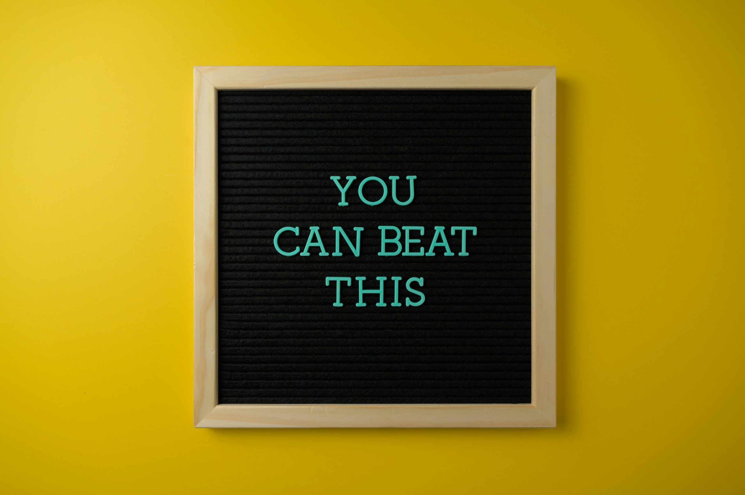 Black letter board with motivational phrase 'You Can Beat This' on vibrant yellow background.